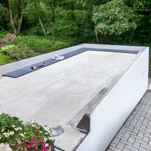 A roof terrace is being built on the concrete roof of a garage next to a house on a slope. To do this, the homeowner simply lays slate grey WARCO terrace tiles on the existing, flat garage roof.