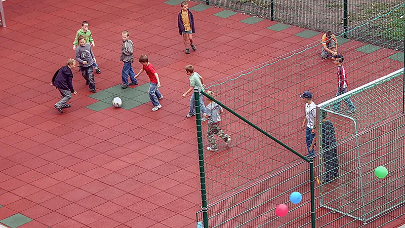 Here we see a nice basketball  field in use, with a few players on the field. A clever use of two colours of tiles has been implemented to make the middle point of the field clear